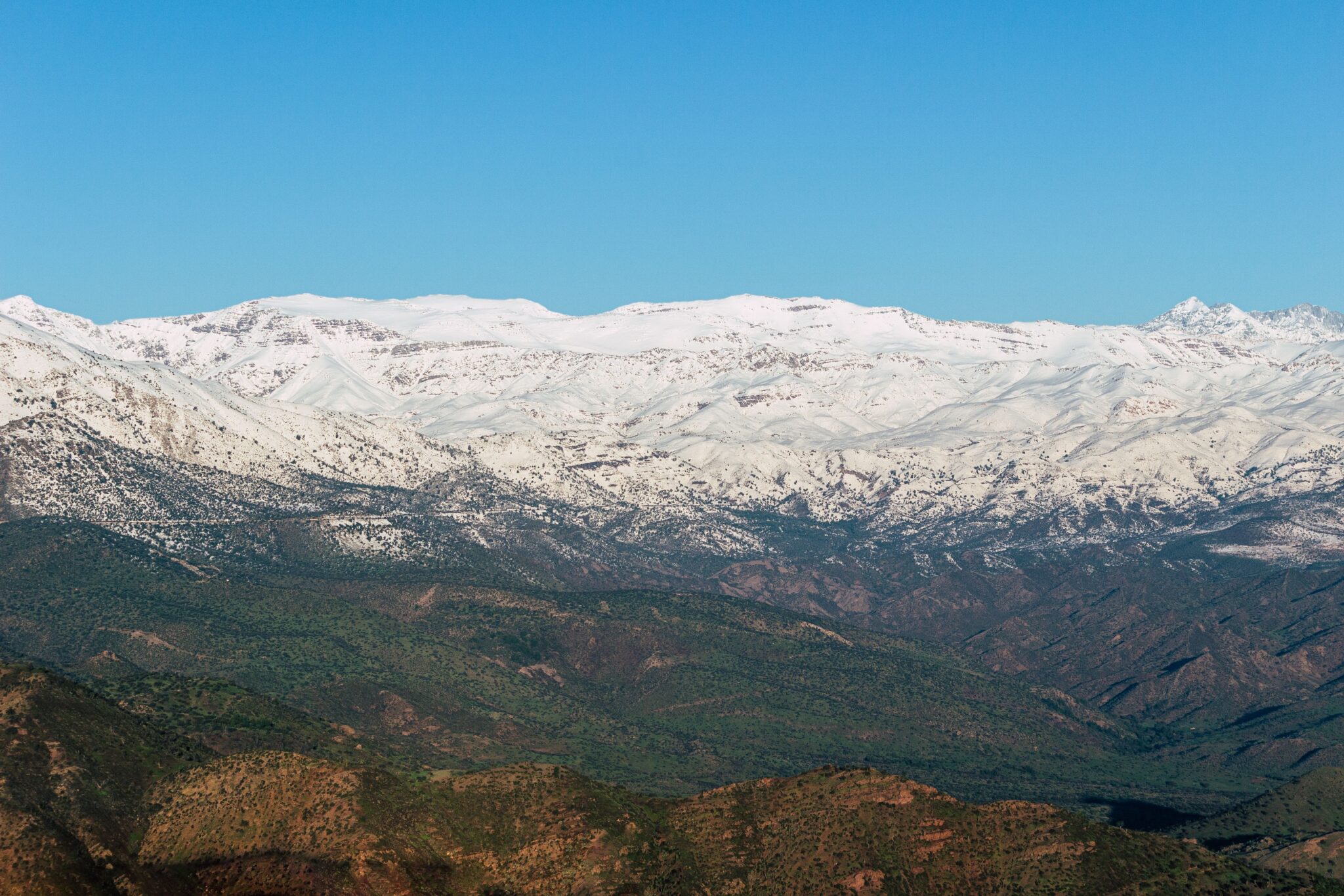 A breathtaking view of the snow-covered Atlas Mountains set against a clear blue sky, showcasing nature's beauty.